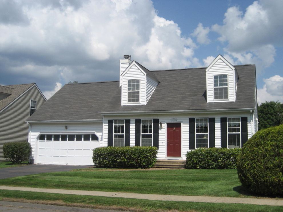 Cape Cod Lumber with Traditional Exterior  and Black Window Shutters Brown Front Door Bushes Cape Cod Dormer Windows Dormers Grass Lawn Shrubs White Exterior White Garage Door White Siding White Window Trim