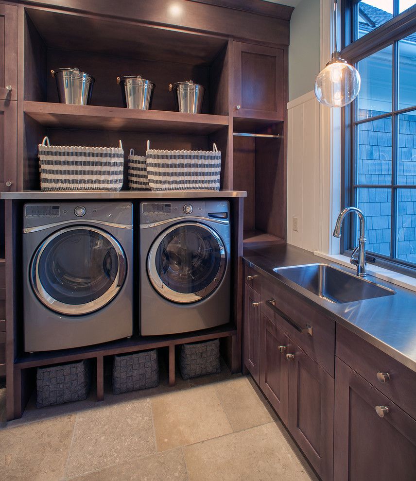 Washer and Dryer Platform with Transitional Laundry Room  and Buckets Built Ins Cubbies Dark Stained Wood Integrated Sink Pendant Light Stainless Steel Counter Stainless Steel Sink Stone Tile Floor Storage Baskets Wainscoting Window